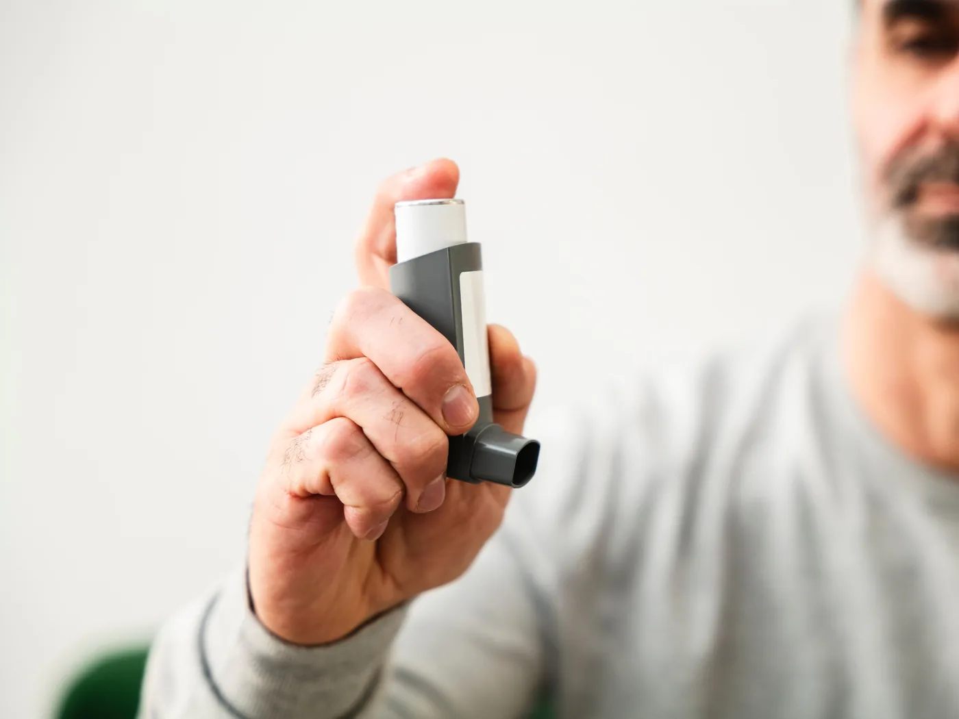 A man holding a metered-dose asthma inhaler toward the camera