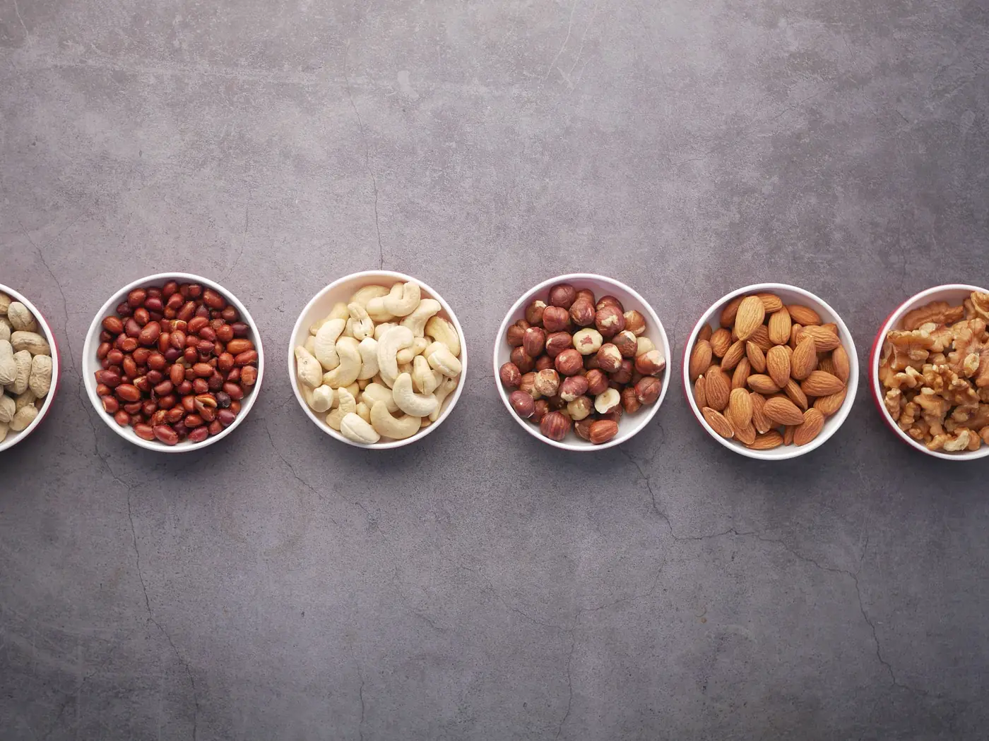 Bowls of peanuts, cashews, hazelnuts, almonds and walnuts on a stone counter