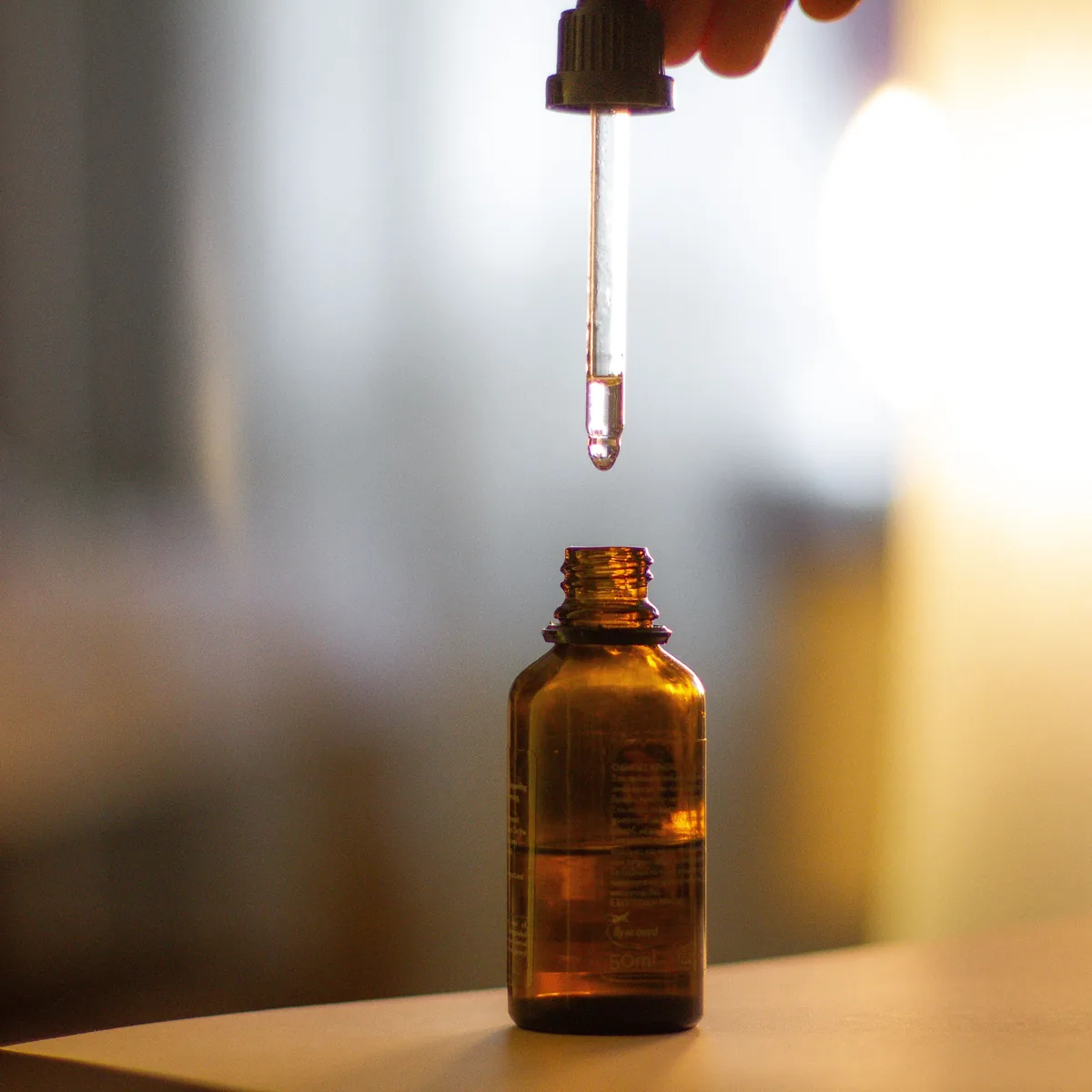 A pipette held above an amber dropper bottle on a table at home